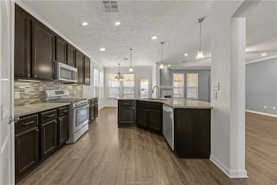 Kitchen featuring dark brown cabinetry, appliances with stainless steel finishes, decorative light fixtures, dark wood-style flooring, and a chandelier