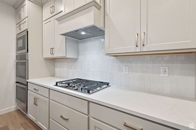 Gourmet Kitchen featuring tasteful backsplash, recessed lighting, white cabinets, light wood-style flooring, built in range, wood hood, and appliances with stainless steel finishes