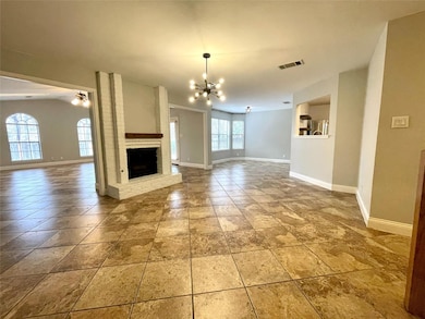 Unfurnished living room featuring plenty of natural light, a chandelier, and a brick fireplace