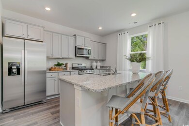 Kitchen with stainless steel appliances, a sink, wood finished floors, gray cabinets, and light stone countertops
