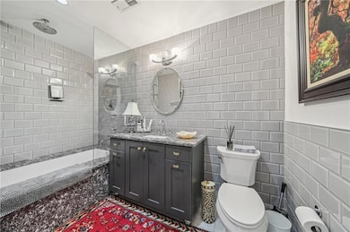 The primary ensuite bathroom features vanity, tile walls, toilet, and tiled shower / bath