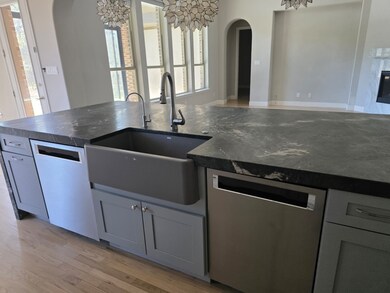 Kitchen featuring arched walkways, stainless steel dishwasher, light wood-style flooring, and dark stone counters