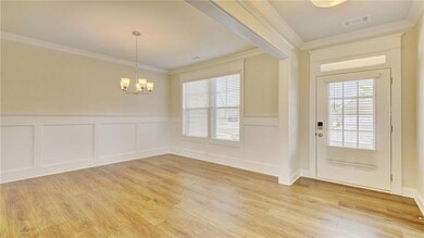 Entrance foyer featuring crown molding, a chandelier, light wood-style flooring, plenty of natural light, and a wainscoted wall