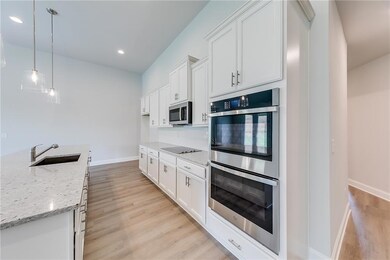 Kitchen with appliances with stainless steel finishes, pendant lighting, light stone countertops, white cabinetry, and light wood-style flooring