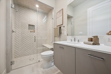 The first-floor shower with frameless glass shower enclosure showcases striking herringbone tile extending to the ceiling and a convenient built-in bench.