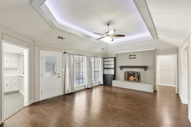 Unfurnished living room with a raised ceiling, dark wood-style flooring, a fireplace, and a ceiling fan