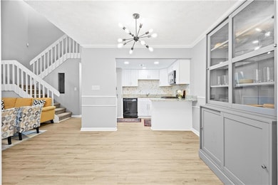 Kitchen featuring open floor plan, a chandelier, light wood-style flooring, white cabinetry, and tasteful backsplash
