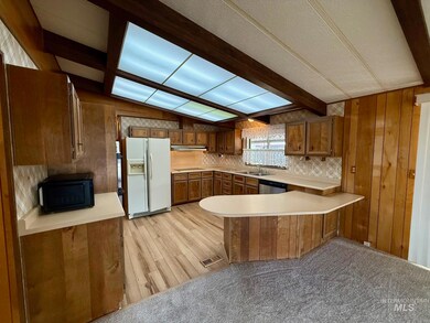 Kitchen with black appliances, a peninsula, light countertops, brown cabinetry, and beamed ceiling
