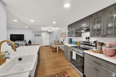 Kitchen with gray cabinets, stainless steel electric range oven, recessed lighting, under cabinet range hood, and light wood-style floors