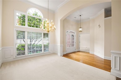 Carpeted entryway with arched walkways, a chandelier, ornamental molding, a wainscoted wall, and wood finished floors