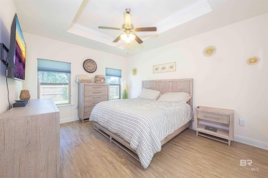 Bedroom with a tray ceiling, light wood-style flooring, ornamental molding, and a ceiling fan