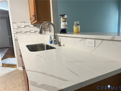 Kitchen with light stone counters, tasteful backsplash, light tile patterned floors, and brown cabinetry