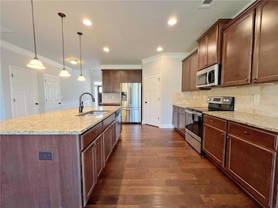 Kitchen featuring stainless steel appliances, ornamental molding, a kitchen island with sink, backsplash, and dark wood-type flooring