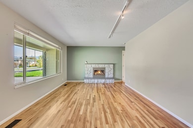 Unfurnished living room with rail lighting, a textured ceiling, a stone fireplace, and light wood-style flooring