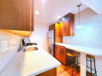 Kitchen featuring freestanding refrigerator, a kitchen breakfast bar, light stone counters, pendant lighting, and brown cabinetry