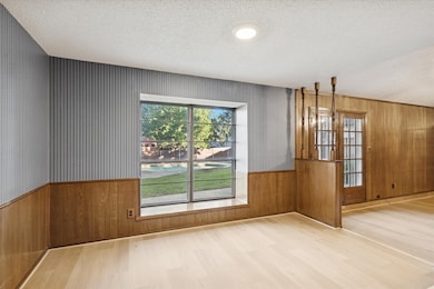 Breakfast room with wooden walls, light wood finished floors, a textured ceiling, and wainscoting