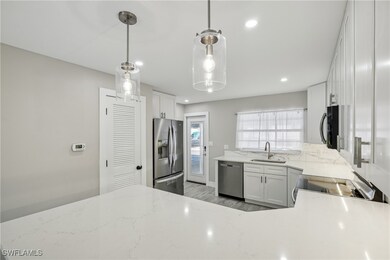 Kitchen with light stone counters, light wood-style flooring, a sink, white cabinets, and appliances with stainless steel finishes