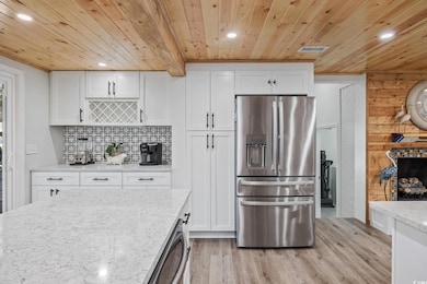 Kitchen featuring stainless steel refrigerator with ice dispenser, white cabinetry, recessed lighting, light stone counters, and light wood-type flooring