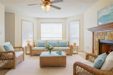 Carpeted living area with a ceiling fan and a warm lit fireplace