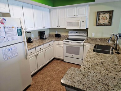 Kitchen featuring white appliances, a sink, white cabinetry, dark tile patterned floors, and light stone counters