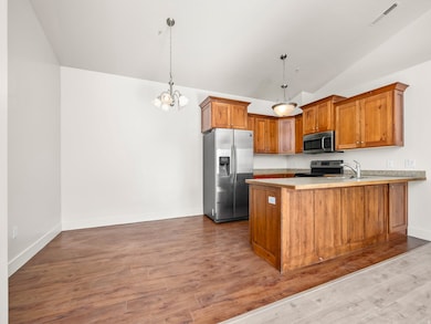 Kitchen featuring brown cabinetry, decorative light fixtures, a peninsula, stainless steel appliances, and light countertops