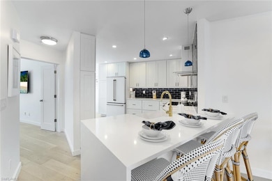 Kitchen with decorative backsplash, white cabinetry, a peninsula, pendant lighting, and high end fridge