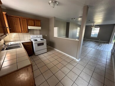 Kitchen featuring ceiling fan, sink, tile counters, electric range, and decorative backsplash