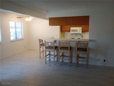 Kitchen featuring tile countertops, brown cabinetry, a kitchen breakfast bar, white appliances, and a peninsula