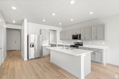 Kitchen featuring stainless steel appliances, light wood-style flooring, a kitchen island with sink, recessed lighting, and light stone countertops