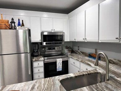 Kitchen featuring stainless steel appliances, light stone counters, and white cabinets