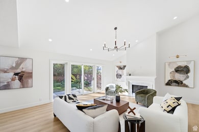 Living room with a premium fireplace, high vaulted ceiling, light wood-style flooring, recessed lighting, and a chandelier
