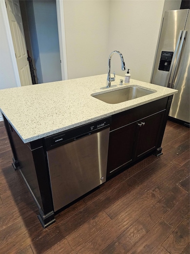 Kitchen featuring fridge, dark wood-type flooring, dishwasher, and an island with sink