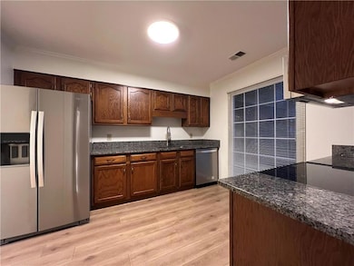 Kitchen featuring stainless steel appliances, crown molding, light wood-style floors, dark stone counters, and dark brown cabinets