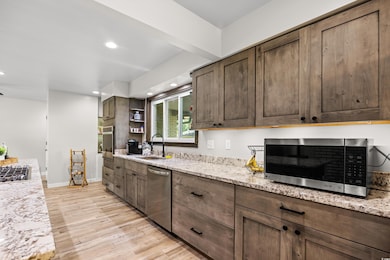 Kitchen with appliances with stainless steel finishes, light wood-type flooring, open shelves, recessed lighting, and dark brown cabinetry