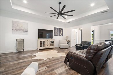 Living room with a raised ceiling, a ceiling fan, recessed lighting, and wood finished floors