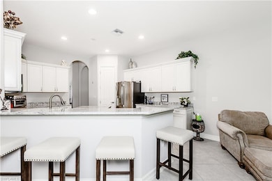 Kitchen featuring stainless steel refrigerator with ice dispenser, a peninsula, white cabinets, a breakfast bar, and recessed lighting