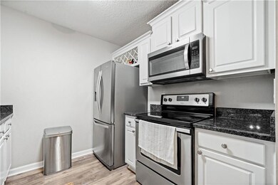Kitchen featuring appliances with stainless steel finishes, a textured ceiling, white cabinets, dark stone counters, and light wood-type flooring