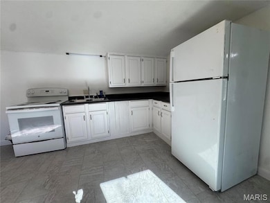 Kitchen with white appliances, dark countertops, white cabinets, and light marble finish floors