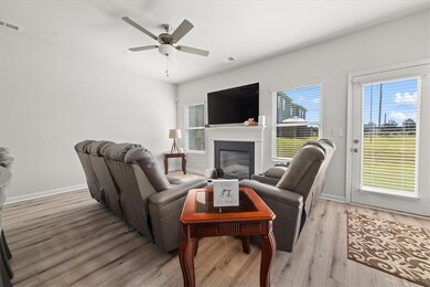 Living area featuring light wood-type flooring, a ceiling fan, and a glass covered fireplace