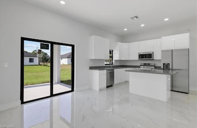 Kitchen with light marble finish flooring, appliances with stainless steel finishes, modern cabinets, a kitchen island, and white cabinets