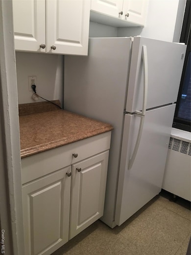 Kitchen featuring white cabinets, freestanding refrigerator, radiator heating unit, and dark countertops