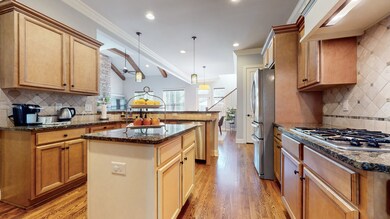 The kitchen features hardwood floors, a tile backsplash, granite counters, a decorative hood, a gas cooktop, an island, and a snacking bar.  The refrigerator is new and remains.