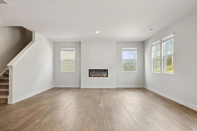 Unfurnished living room with wood finished floors, stairway, baseboards, a large fireplace, and recessed lighting
