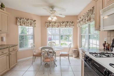 Kitchen with gas range, white microwave, light tile patterned floors, a ceiling fan, and cream cabinets