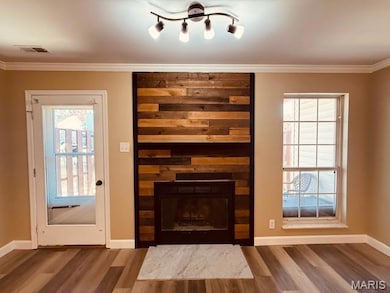 Unfurnished living room featuring a fireplace, wood finished floors, and crown molding