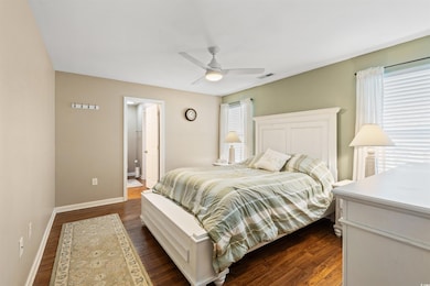 Bedroom featuring multiple windows, dark wood-style flooring, ensuite bath, and a ceiling fan