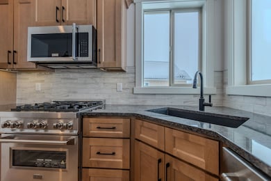 (PHOTO OF SIMILAR HOME)Kitchen featuring appliances with stainless steel finishes, plenty of natural light, tasteful backsplash, and dark stone countertops