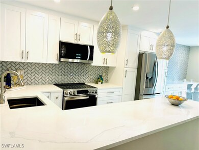 Kitchen featuring appliances with stainless steel finishes, white cabinetry, light wood-style tile floors, light  countertops, and pendant lighting
