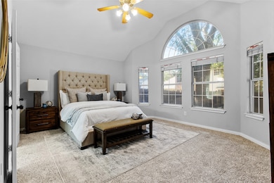 Carpeted bedroom with a ceiling fan and high vaulted ceiling