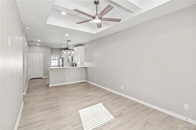 Unfurnished living room featuring a raised ceiling, ceiling fan, and light wood-type flooring